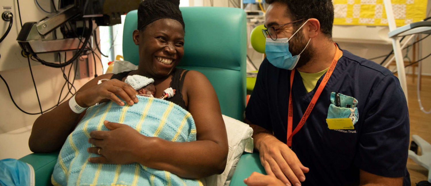 Mother holding newborn laughing with health professional at hospital