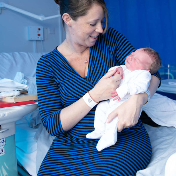 Mother holding baby in arms and smiling in maternity ward