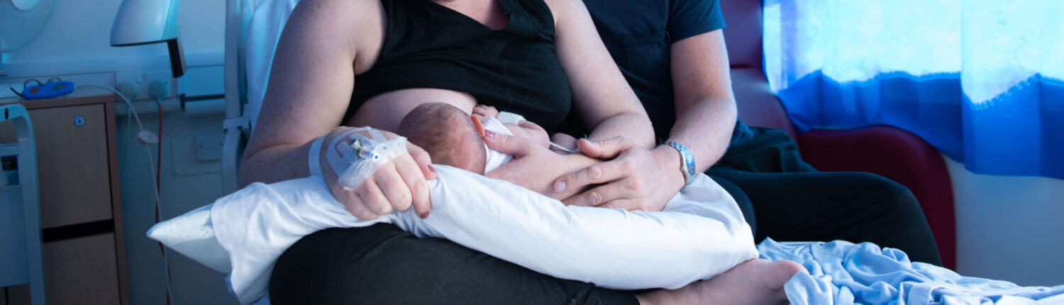 A mother breastfeeds her newborn in the maternity unit alongside the father