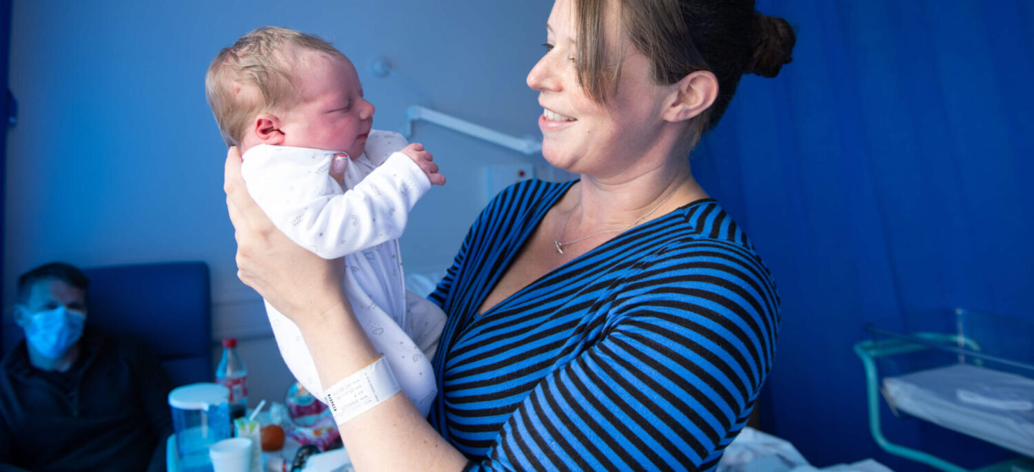Mother holding baby in arms and smiling in maternity ward