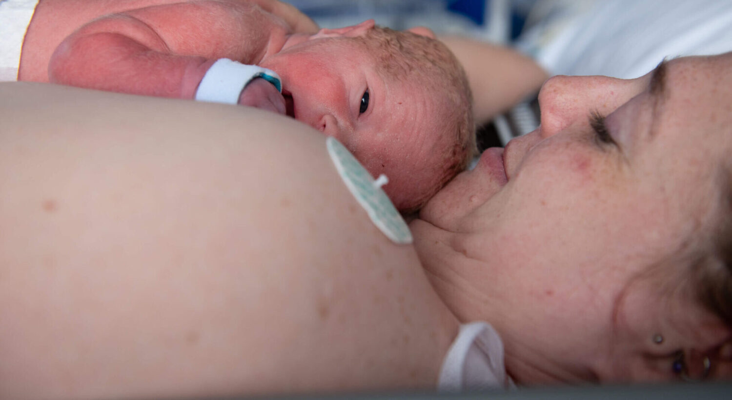 A mother holds her newborn infant in skin-to-skin contact on the maternity wing.
