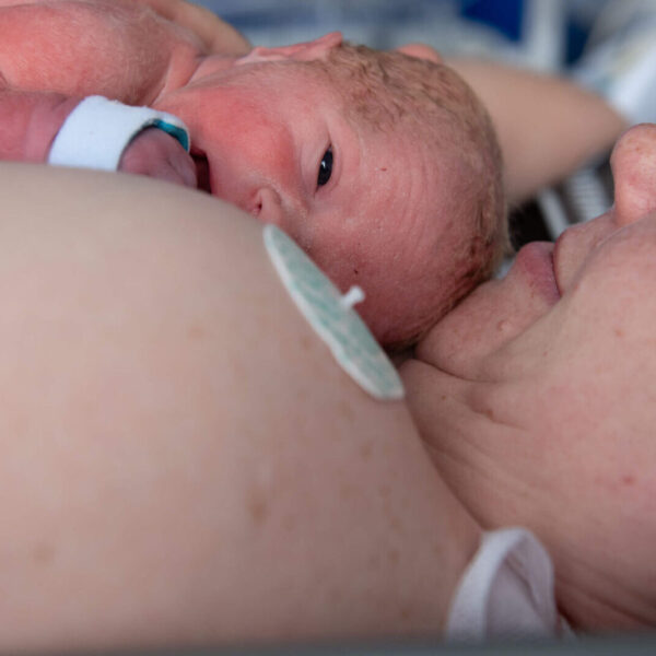 A mother holds her newborn infant in skin-to-skin contact on the maternity wing.