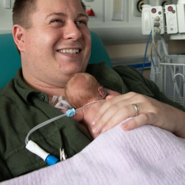 A father of twins born premature holds his infant in skin-to-skin contact on the neonatal unit.