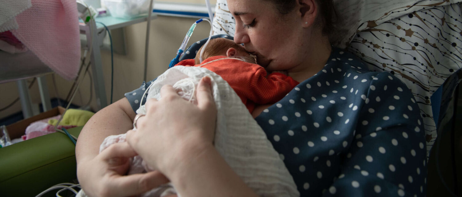 A mother holds one of her twins born premature in skin-to-skin contact on the neonatal unit.