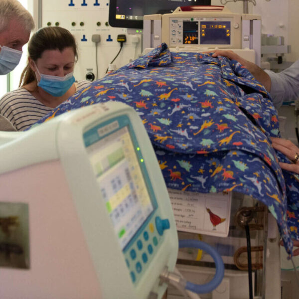 Extended family gather around an incubator in a neonatal unit.