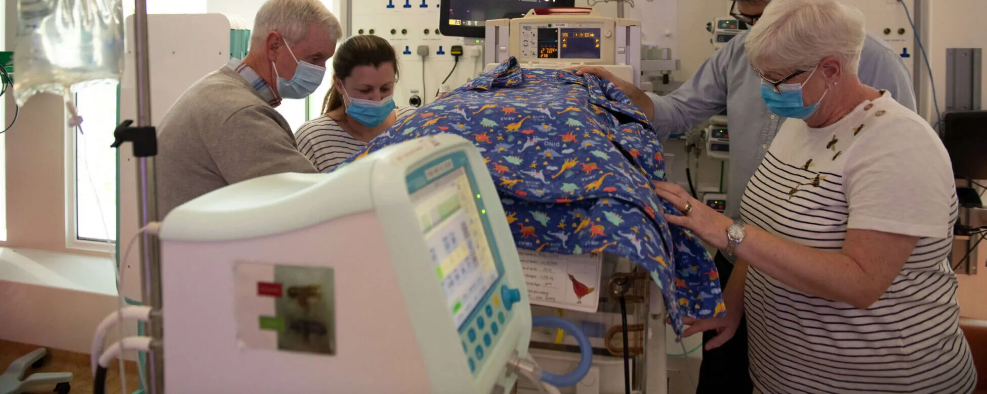Extended family gather around an incubator in a neonatal unit.