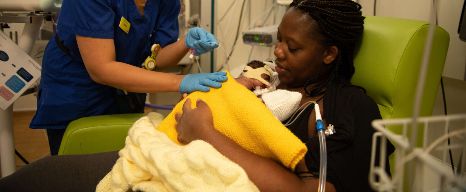 A mother of twins holds her babies in skin-to-skin contact on the neonatal unit with the support of a healthcare professional.