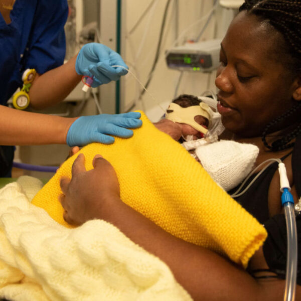 A mother of twins holds her babies in skin-to-skin contact on the neonatal unit with the support of a healthcare professional.