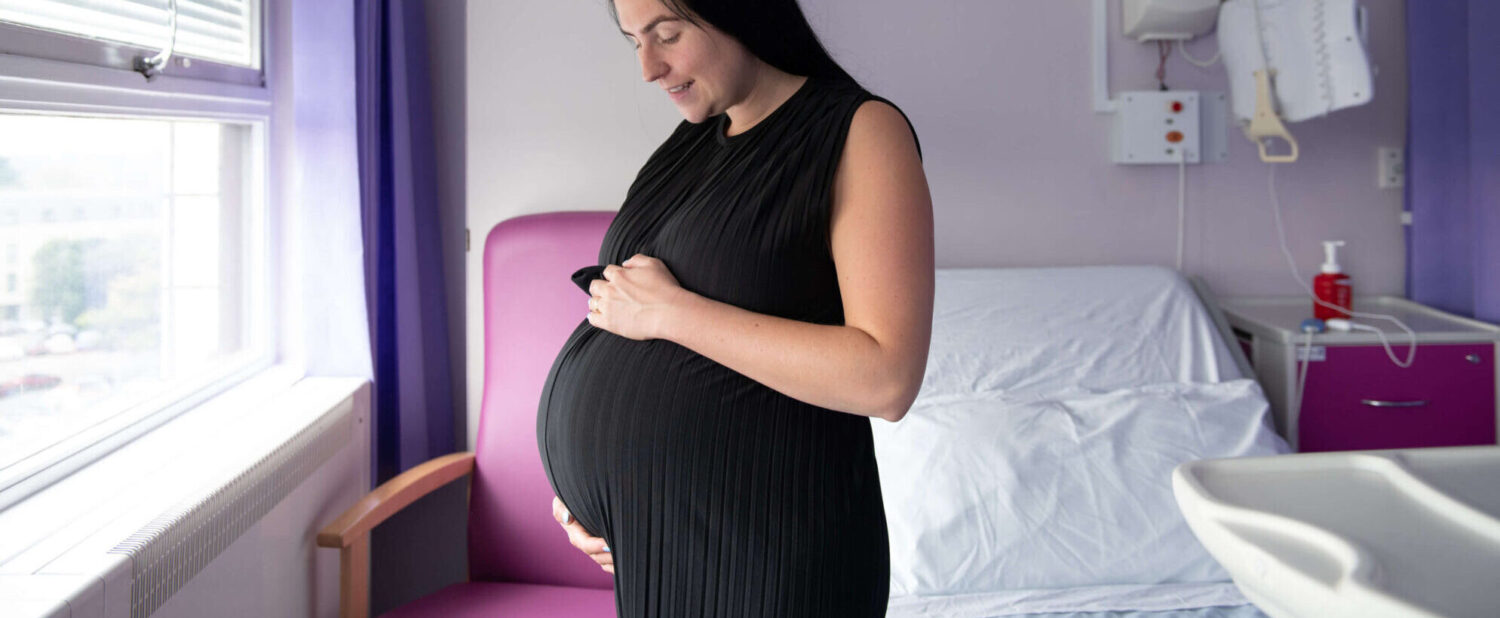A pregnant mother-to-be smiles at her bump in the maternity unit.