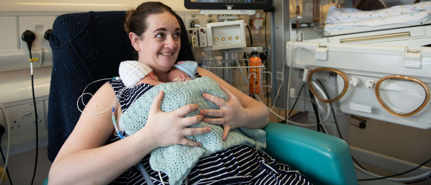 A mother smiles as she holds her twins born premature in skin-to-skin contact on the neonatal unit.