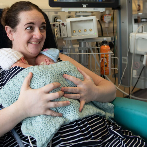 A mother smiles as she holds her twins born premature in skin-to-skin contact on the neonatal unit.
