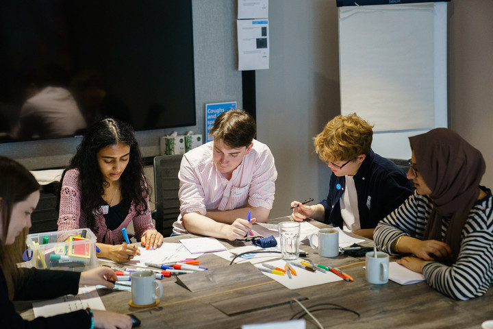 Five young people sit around a table working with pens and paper.