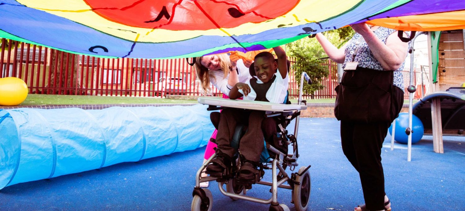 A boy in a wheelchair playing the parachute playground game with teachers
