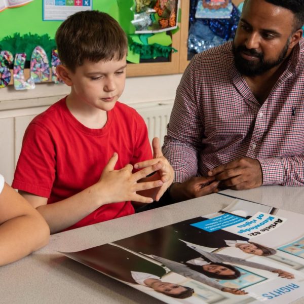 A teacher supporting two pupils, looking at a UNICEF poster and discussing children's rights
