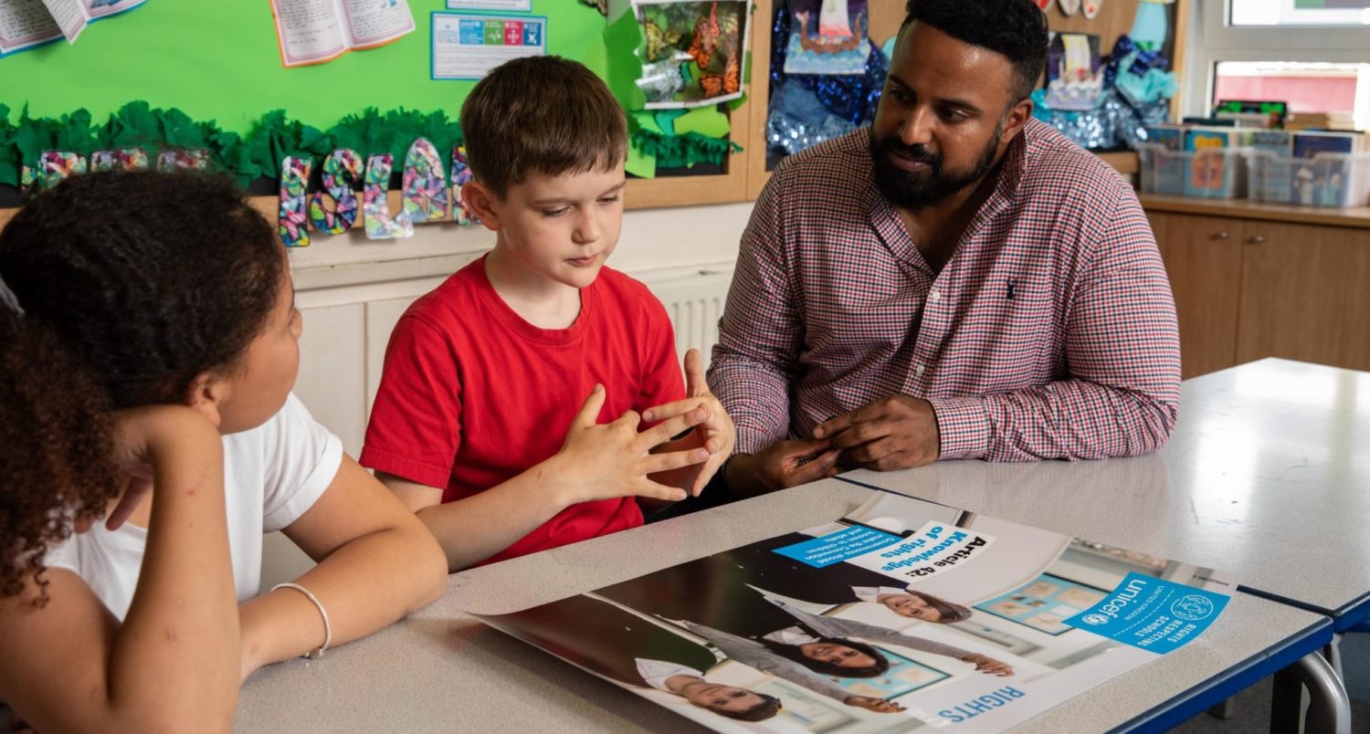 Teacher and two pupils looking at a UNICEF poster, discussing children's rights