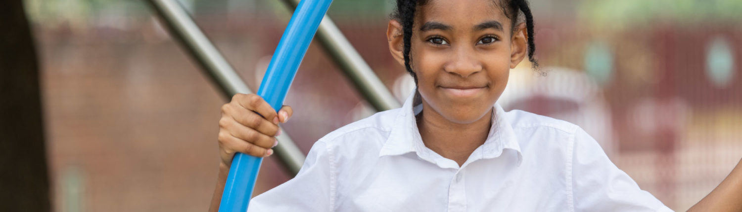 A girl smiling at a camera while playing at a playground at school