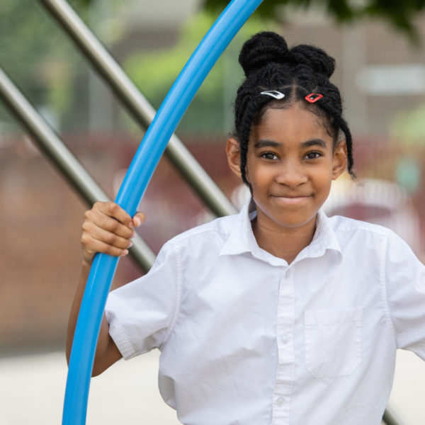A girl smiling at a camera while playing at a playground at school