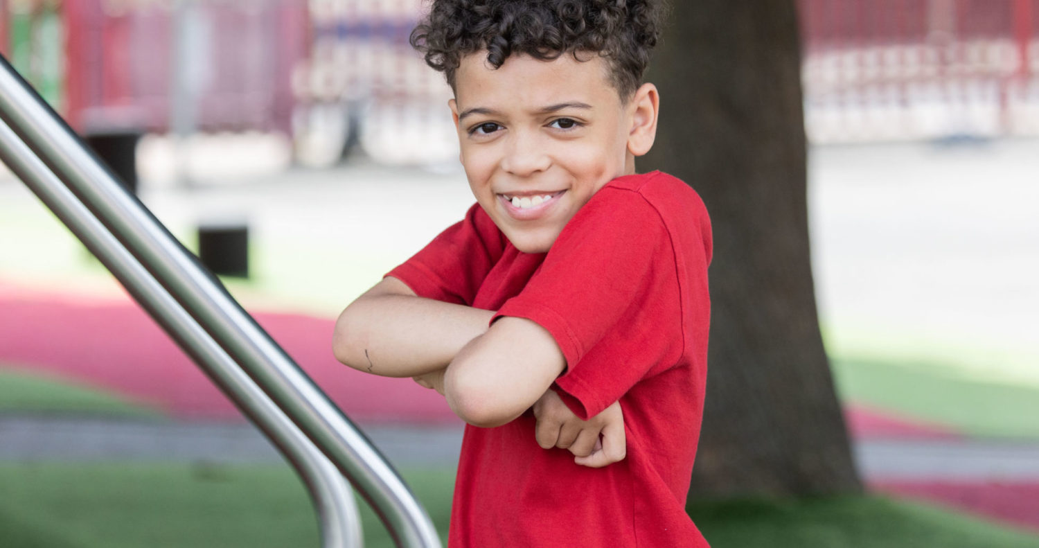 a boy in red t-shirt posing at a school playground