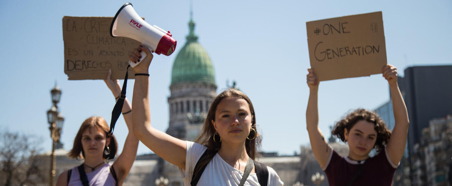 Three young people campaigning for climate action, holding signs and a megaphone.