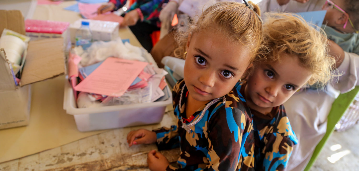 Two girls wait in line at a temporary medical centre in Iraq. Unicef/2016/Kuzaie