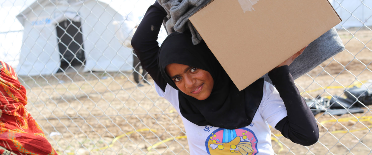 A smiling girl carries blankets and a box with winter supplies at a camp in Iraq. Unicef/2016/Anmar
