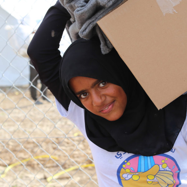 A smiling girl carries blankets and a box with winter supplies at a camp in Iraq. Unicef/2016/Anmar