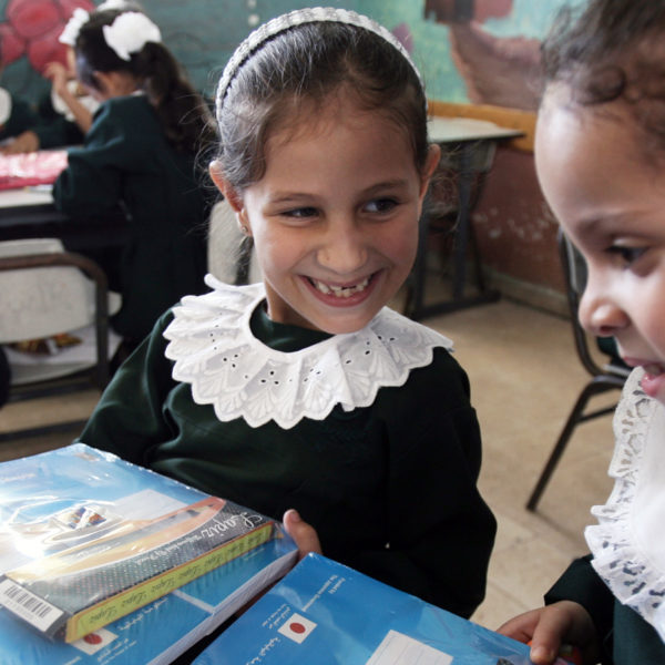 Two smiling girls hold new stationery kits from a Unicef distribution at their school in Gaza. Unicef/2014/El Baba
