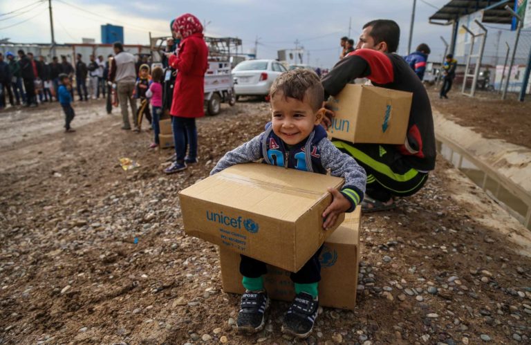 How does Unicef source winter clothes for Syrian children? A young boy clutches a box of Unicef winter clothing kits.