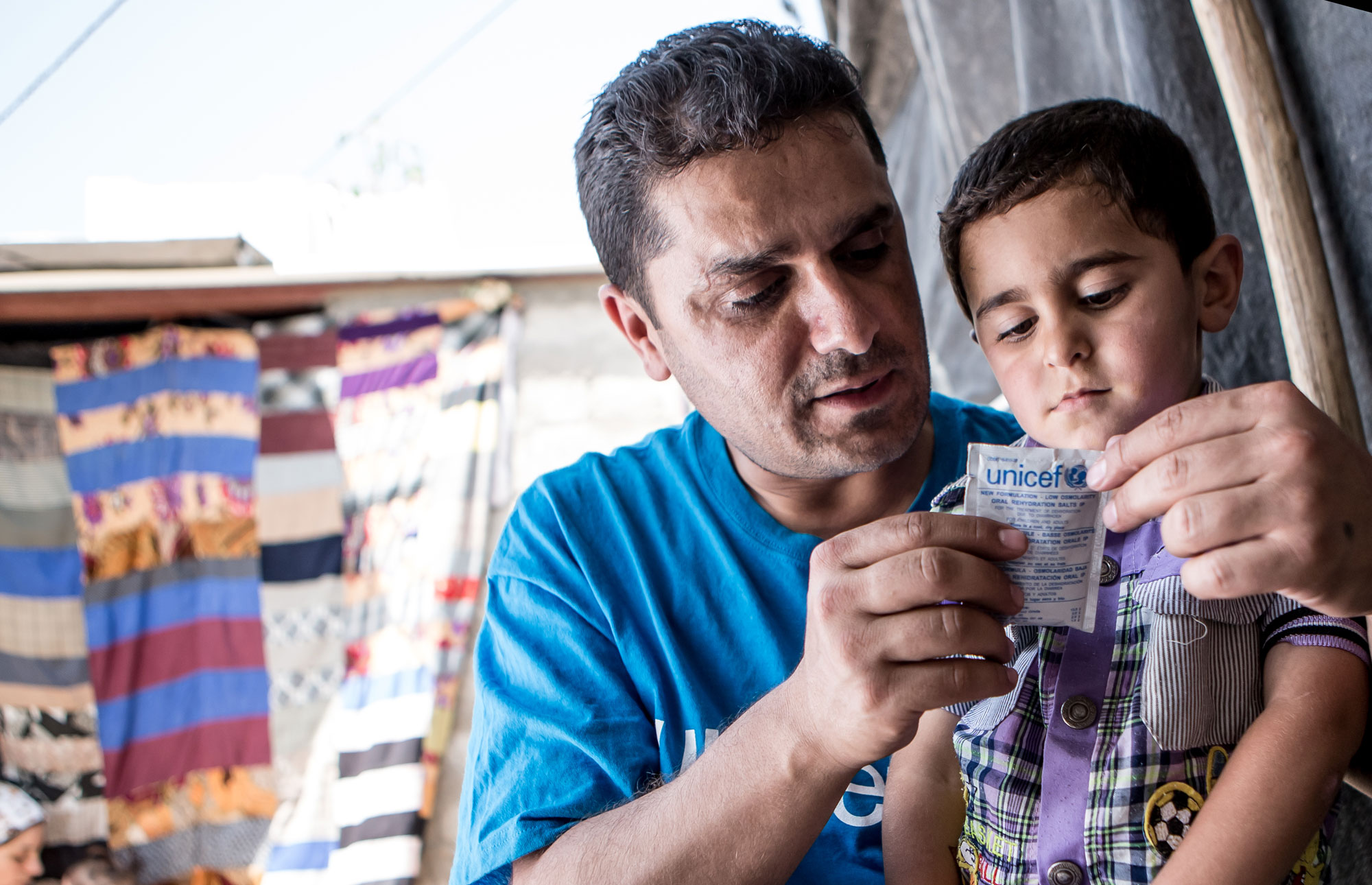 Iraq, May 2013. UNICEF worker Abduljabar prepares oral rehydration salts for four year old Ahmed. Ahmed lives with his brother and parents in a small room amongst five other families in the Domiz refugee camp in Northern Iraq. Domiz is situated near the city of Dohuk, about forty miles from the Syrian border. Approximately 40,000 Syrians are living here, in facilities provided for around half that number. Unicef 2013 Schermbrucker