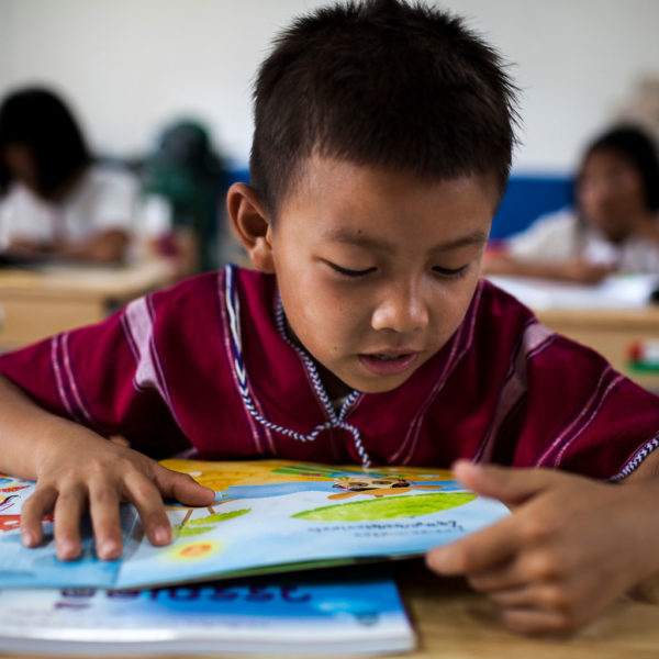 A young boy reads a book in a school classroom. Photo: UNICEF Thailand/2015/Prommarak