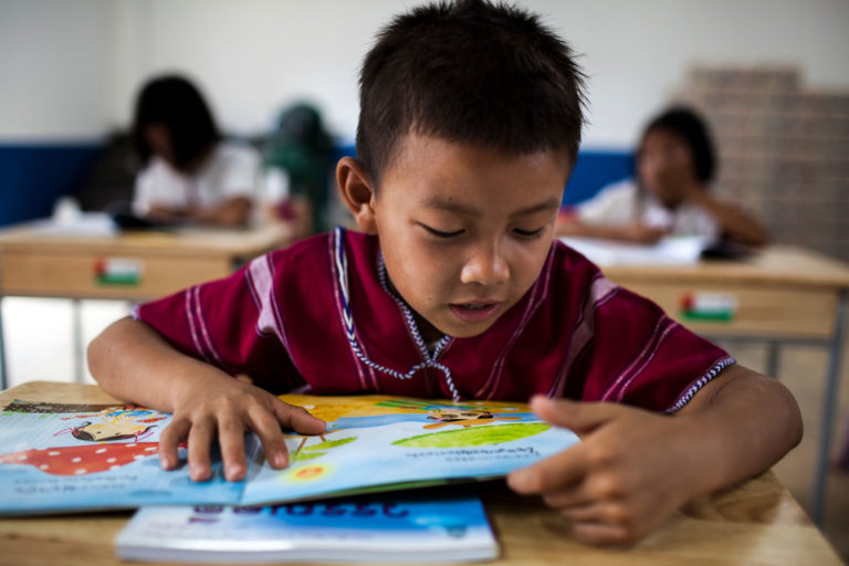 A young boy reads a book in a school classroom. Photo: UNICEF Thailand/2015/Prommarak