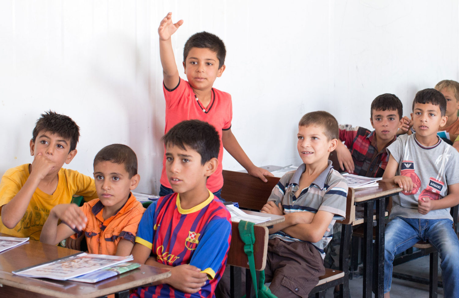 A classroom of boys where one boy is standing with his hand held up.