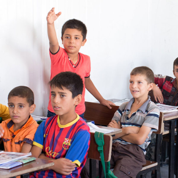 A classroom of boys where one boy is standing with his hand held up.