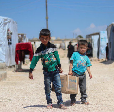 On 29 April 2020 in the Syrian Arab Republic, brothers Ahmad (left), 7, and Saad, 5, help their mother carry their newly received family hygiene kit back to their tent in Fafin camp, northern rural Aleppo.