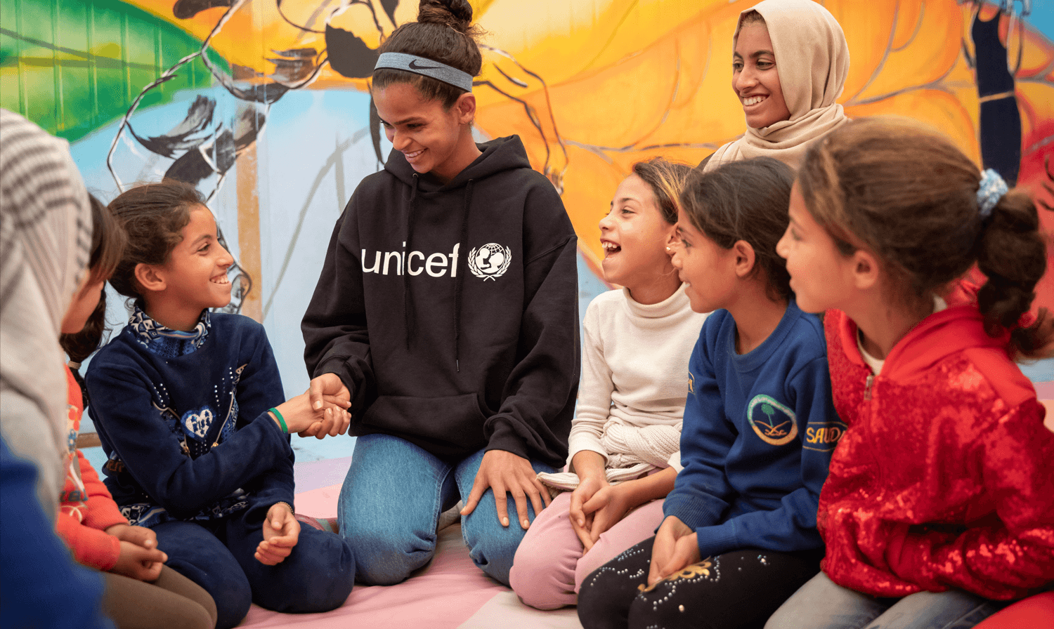 Ramala Ali shakes the hand of a young girl with other young girls looking on and smiling.