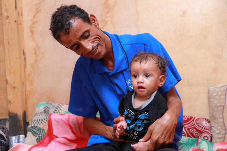 Yahya holds his child in the Al Sha'ab camp.