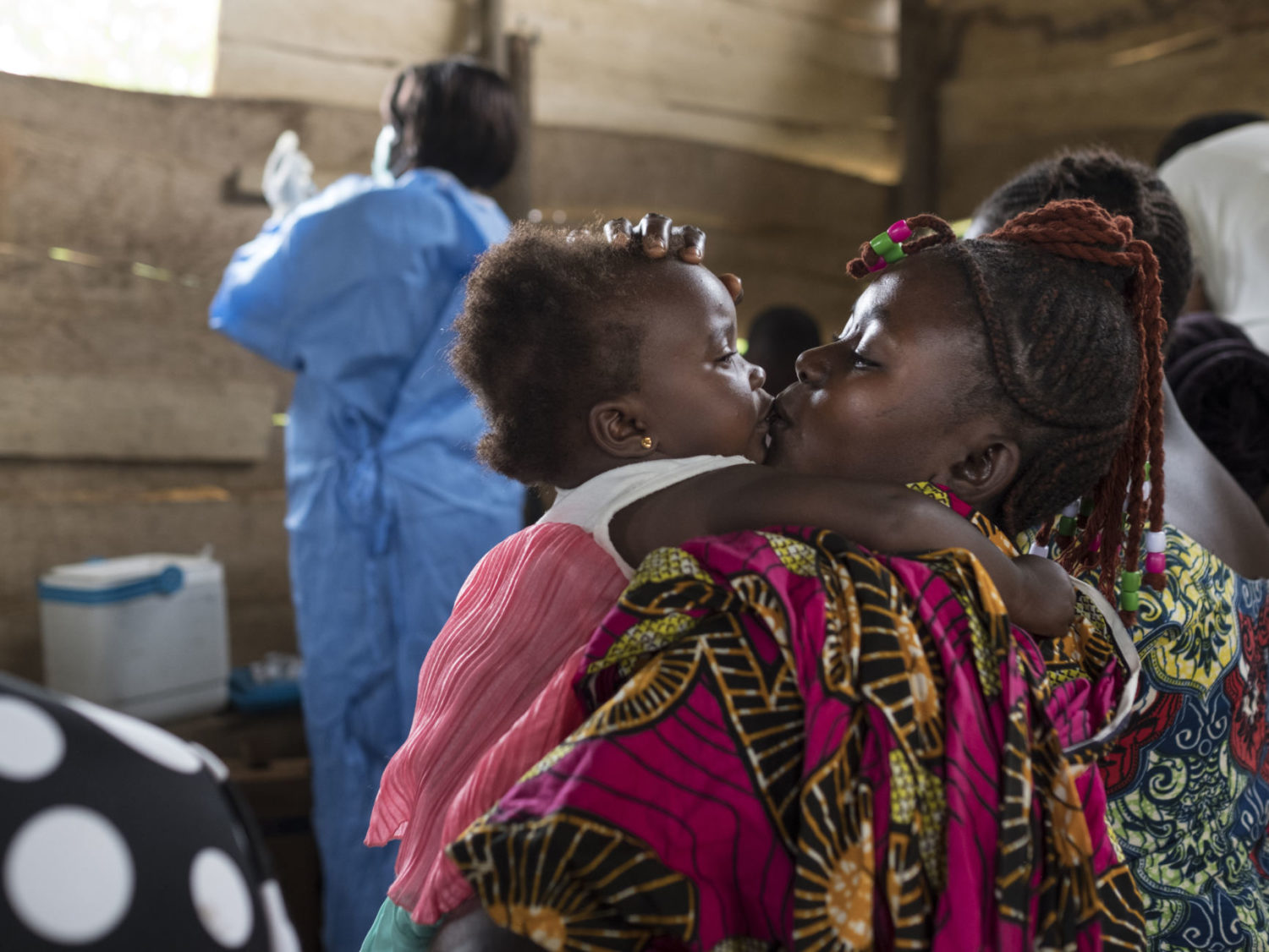 A mother kisses her daughter at a regularly scheduled, UNICEF-supported immunization clinic in the village of Kuka on the outskirts of Beni in North Kivu province, Democratic Republic of the Congo on 21 October 2019. Despite the recent Ebola outbreak and its toll on the community, 80 children have shown up to receive vaccines against a number of diseases, including polio, yellow fever, tetanus and diphtheria. UNICEF provides the vaccines, cold storage and transport for the health workers, in addition to logistical and technical support.
