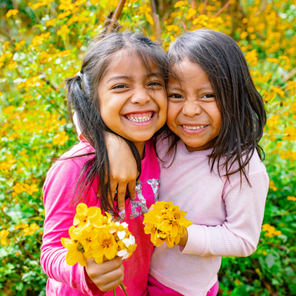 Two children smiling together in a field at the back of their house in Olintepeque, Quetzaltenango, Guatemala.