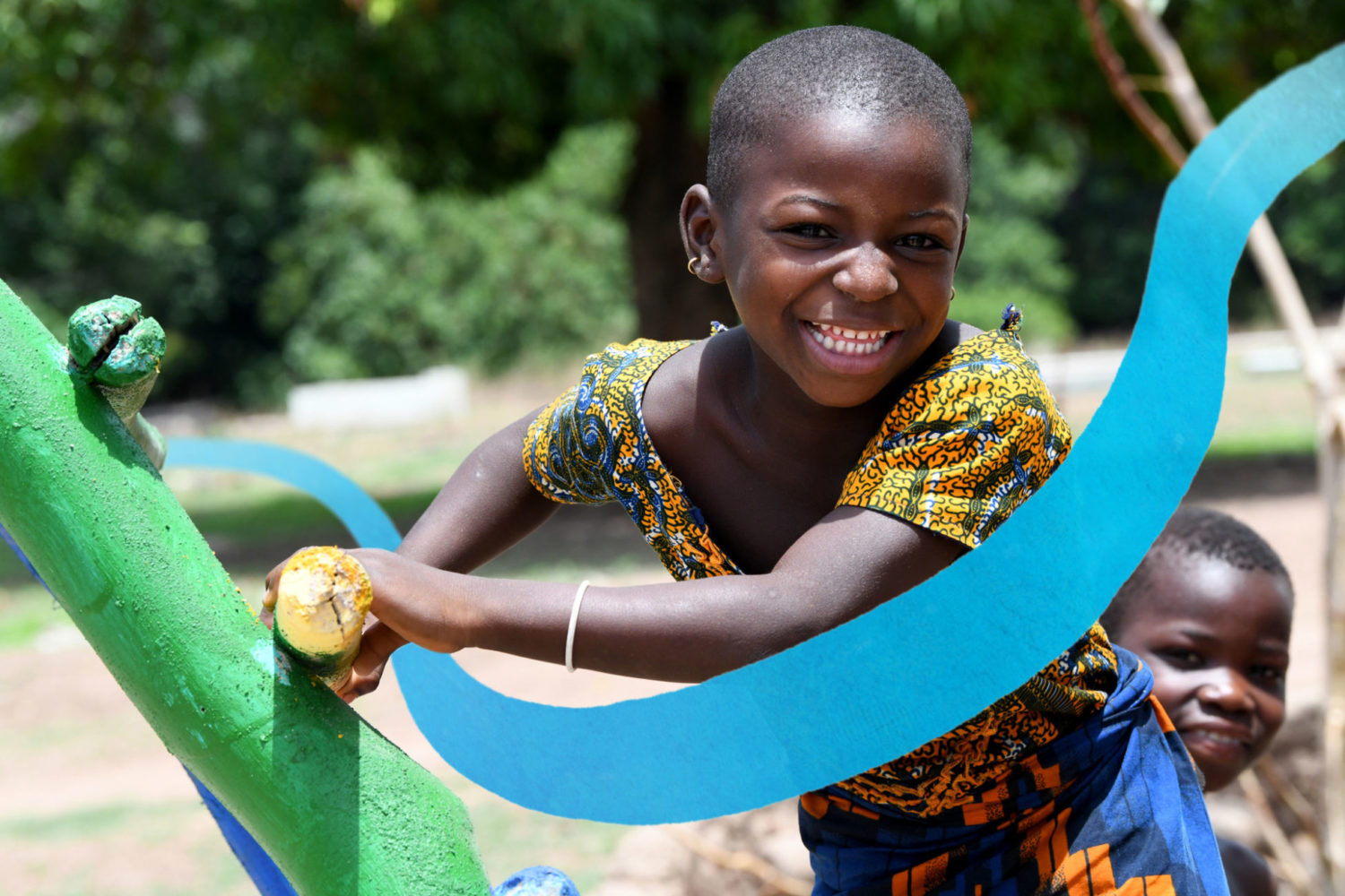 A smiling child plays in the park. A UNICEF-blue streak is overlayed across the image as part of the Gift in Will branding.