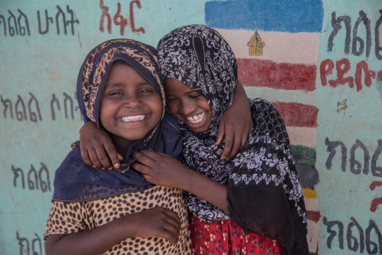 2 girls laughing while one has her arm around the other
