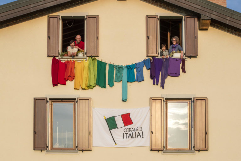 Coloured clothes hang between the windows of house, arranged like a rainbow