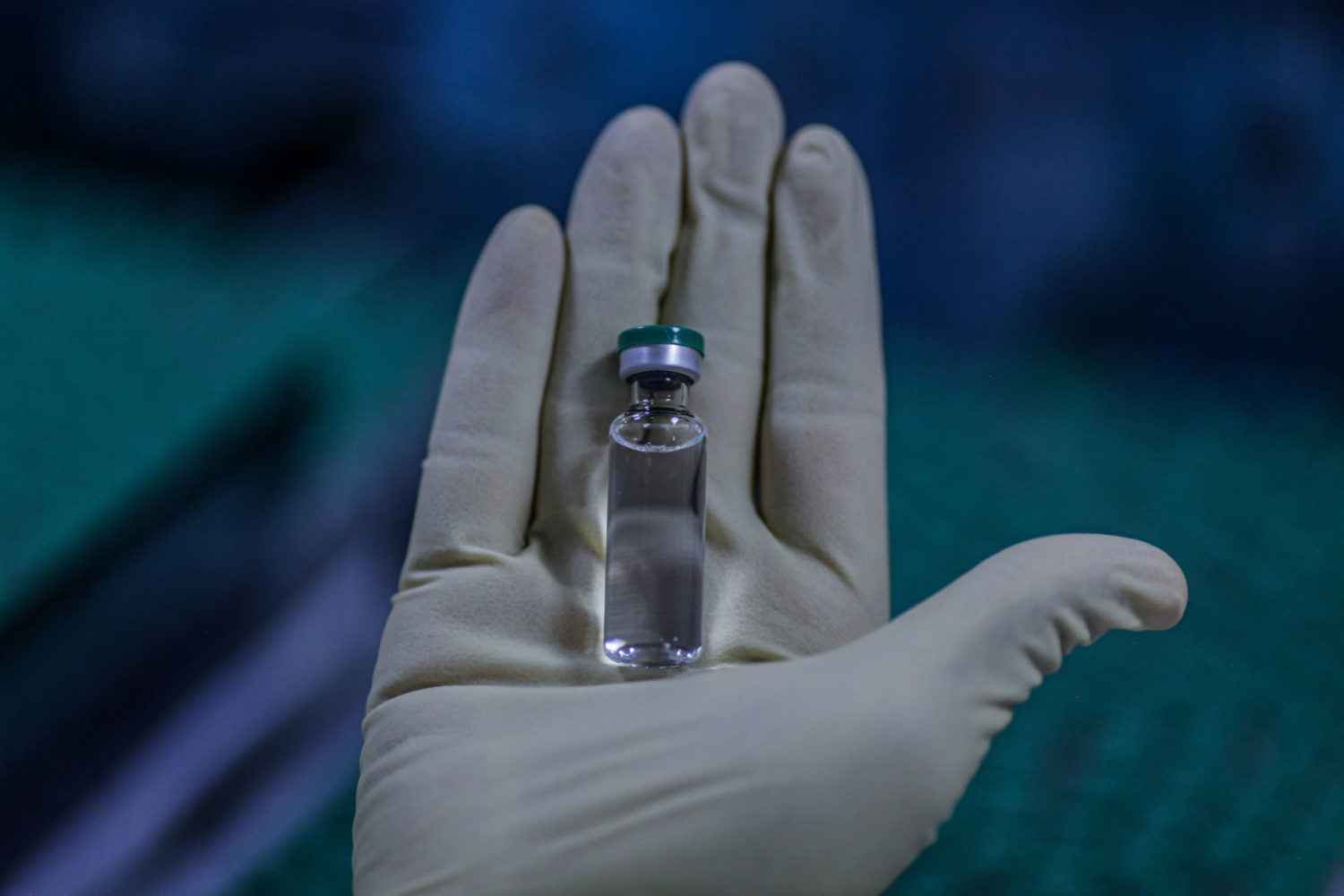 Gloved hand holding a vaccine vial.