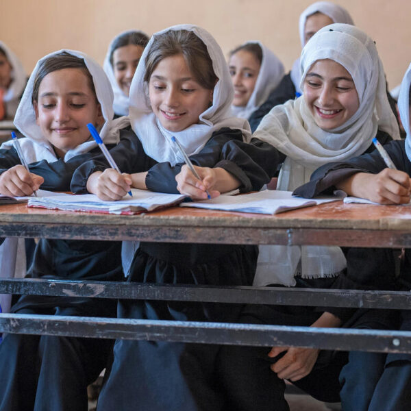 A group of four schoolgirls smile at their desks while writing.