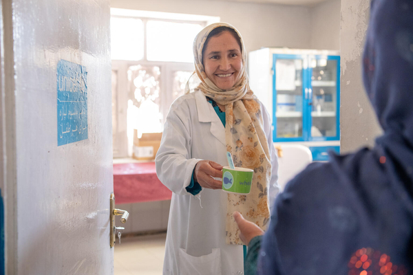 A smiling nurse hands over a cup of therapeutic milk to a mother.