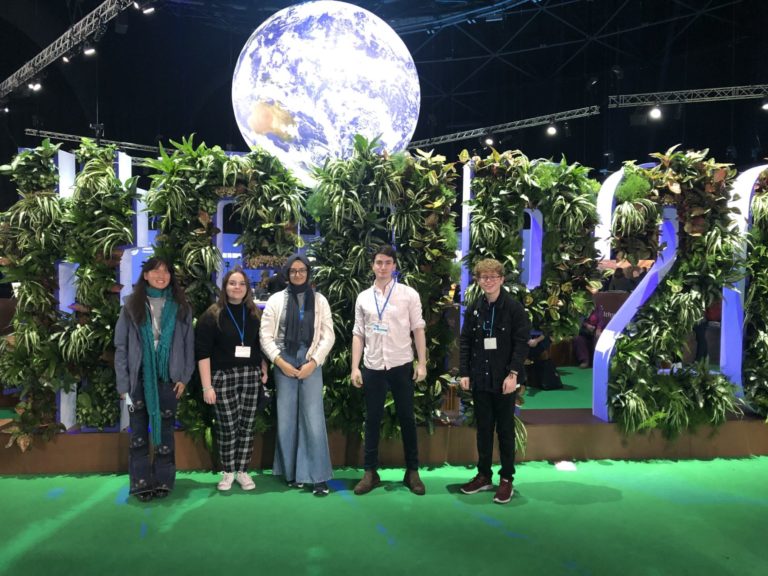 Five young people stand in front of the COP26 sign