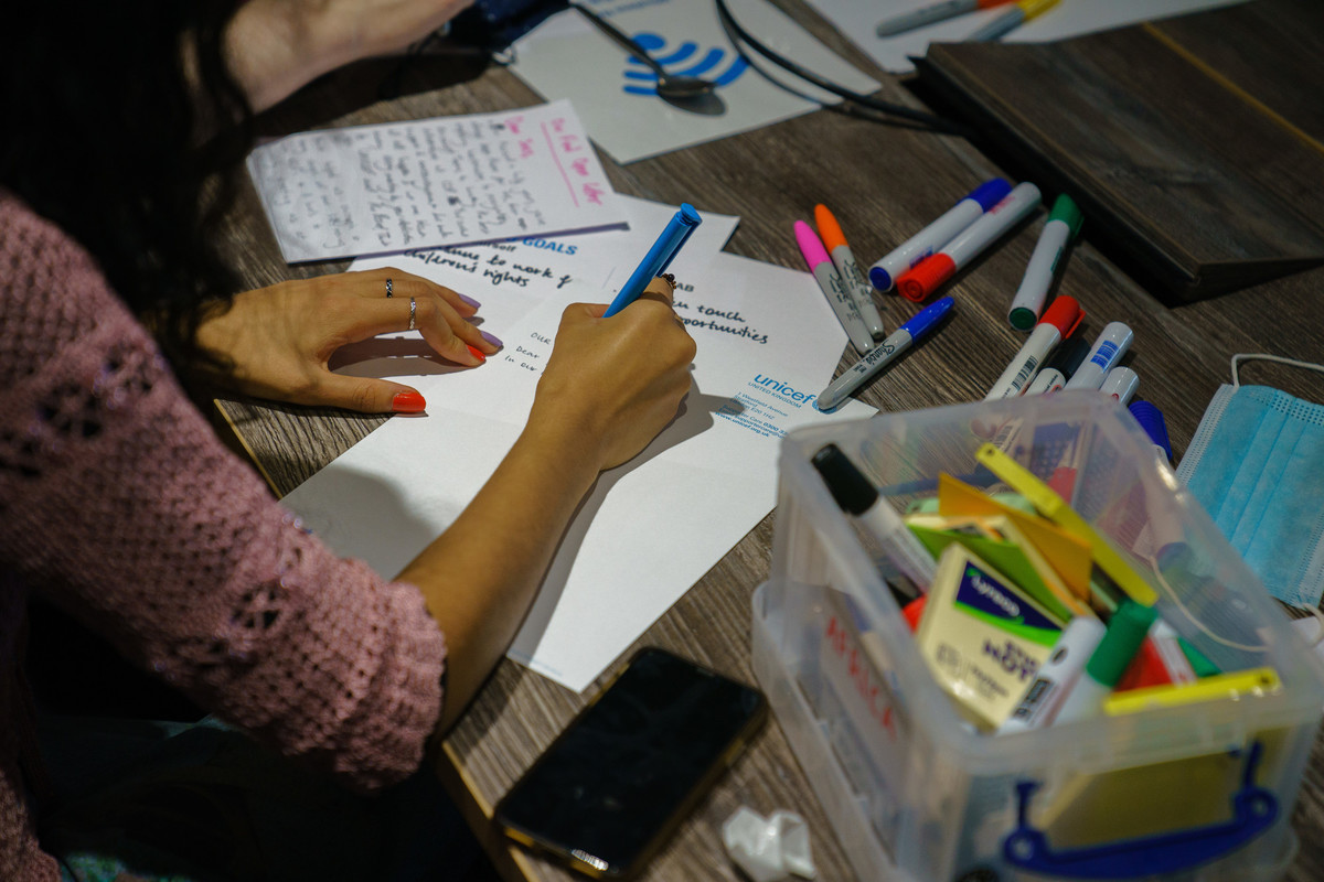 No faces are shown, but young people's hands are shown, writing a letter on UNICE UK paper