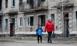 A woman with a boy walk past an old destroyed building in small town of Krasnogorivka. in Ukraine