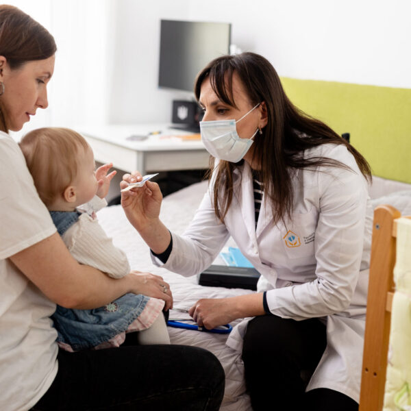 During a home visit, family nurse Nadiia Bezpaliuk examines 1-year-old Solomiia while her mother Olena holds her close.