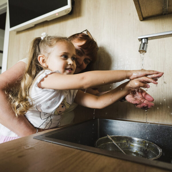 Four-year-old Masha washes her hands at home while her mother Oksana assists her.