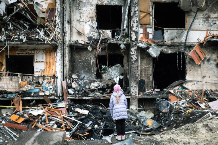 A child stands in front of an apartment building which was heavily damaged during conflict in Ukraine